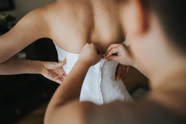 The bride's dress being buttoned at the back