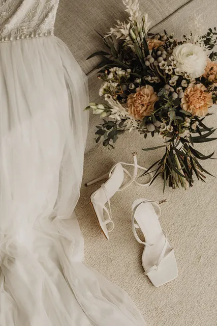 Bridal bouquet and white sandals beside the gown on linen